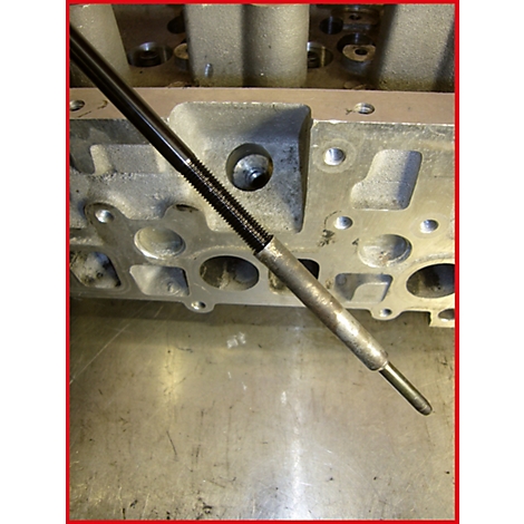 Nahaufnahme einer Zündkerze, die in den Zylinderkopf eingesetzt wird. Der Kopf und die Werkzeuge bestehen aus Metall.